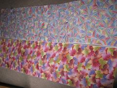 Two long strips of fabric are laid out side-by-side, one with a pattern of colorful leaves on an orange background and the other with a swirling geometric pattern in shades of blue and pink.