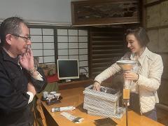 남자와 여자가 테이블에 서 있습니다. 여자는 상자가 쌓여 있는 위에 깔때기 모양의 물체를 잡고 있습니다.