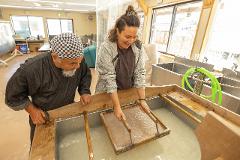 An older man and a younger woman work together in a workshop, demonstrating the process of making Japanese paper.