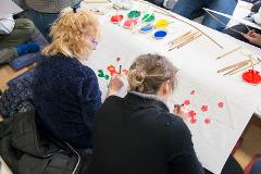 Two women are participating in a traditional Japanese Yuzen dyeing workshop, creating floral designs on fabric with brushes and paints.