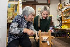 Two women are working with a wooden contraption that spins thread.