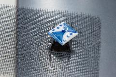A blue and white diamond-shaped ceramic piece is placed on a dark object atop a metal mesh.