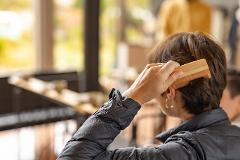 Experience the Craftsmanship of the Oroku Comb born in Kiso A person combs their short brown hair with a wooden comb in a bright, blurry setting.