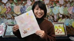 A smiling woman holds up a piece of handmade washi paper with autumn leaf and star decorations.