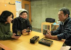 Use Premium Shark Skin and Traditional Lacquer to Craft a Masu Cup near Inuyama Castle Three people are seated at a wooden table looking at small black lacquer boxes with some items inside.