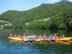 A group of people are kayaking on a lake surrounded by lush green mountains under a clear blue sky.