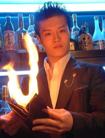 A man in a suit stands in front of a bar, holding a wallet engulfed in flames.