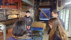 A group of people is gathered inside what appears to be a production facility, possibly for food or beverage, with machinery and equipment visible in the background.