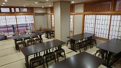 The image shows a Japanese-style room with tatami mats, low tables, and wooden chairs, set up for a tea ceremony experience.