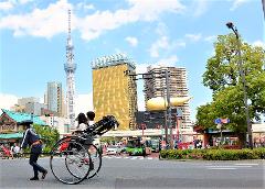 A rickshaw driver pulls a rickshaw with passengers past Tokyo Skytree and modern buildings.