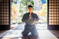 A young person in traditional Japanese attire kneels in prayer before an open doorway with a garden view.