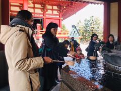 People are gathered at a purification fountain outside a temple in Tokyo, with some scooping water to wash their hands.