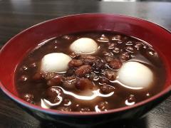 A close-up shot of a red and black bowl filled with Anmitsu, a Japanese dessert consisting of white mochi, red bean paste, and a light sweet sauce.