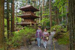Experience the Excellence of Japanese Silk: Handwoven Ina Tsumugi Two women in traditional kimonos walk along a gravel path in a forest towards a multi-tiered wooden pagoda, surrounded by lush greenery and moss-covered stones.