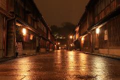 A wet, cobbled street illuminated by lanterns, lined with traditional wooden buildings, at night in Kanazawa.