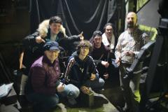 A group of six people are posing for a photo in a workshop, with two individuals in the foreground holding metal tools.