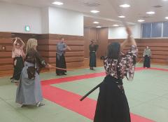 Ľudia praktizujú japonské bojové umenia v dojo, držia drevené meče a nosia tradičné oblečenie hakama a keikogi.