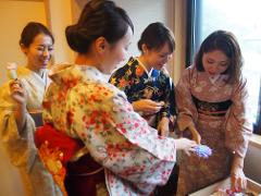 四位身着和服的女子正在检查配饰，面带微笑，全神贯注，似乎在为一个特殊的场合做准备。