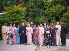 一群 14 名身着传统和服的日本人在郁郁葱葱的绿树前合影。