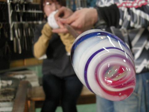 A glassblower is shaping a swirling, colorful glass ornament.