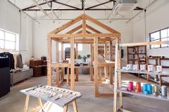 A workshop space with a wooden frame structure, shelves of tea and other items, and a table displaying cutlery.