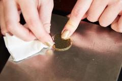 A close-up shot captures a person's hands, adorned with sparkly gold nail polish, working on a circular gold-colored accessory with a textured surface.