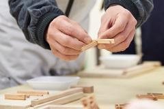 A close-up of hands assembling wooden pieces for a screen.