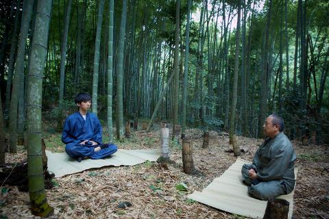两名男子在竹林中冥想，面对面坐在垫子上。
