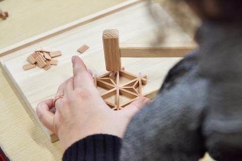 Niigata 10:30AM Kumiko Coaster Crafting & Factory Visit A person's hands assemble a wooden puzzle with a mallet on a workbench.