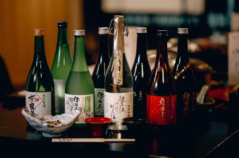 Kitakata 2-Day Sake & Lacquerware Tour with Onsen Stay A variety of sake bottles are artfully arranged on a dark surface with small dishes of food and chopsticks, suggesting a tasting or dining experience.