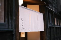 A traditional Japanese restaurant's white noren curtain hangs over an entrance, displaying Japanese calligraphy and the word "Sushi."