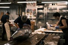 Three men work with a large tuna in a fish market, preparing it for sale or consumption.