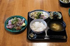 A traditional Japanese breakfast of raw fish, rice, miso soup, and assorted side dishes is presented on a wooden table.