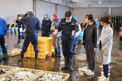 A group of people stand around crates of fish at a market, with some engaged in conversation.
