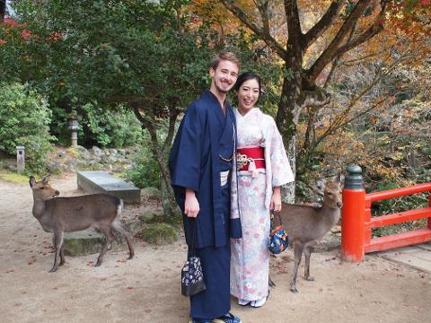 一对身着日本传统服装的夫妇与两只鹿在秋叶掩映的公园里合影。