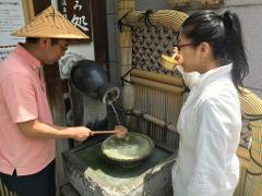 Two people are using a traditional Japanese purification fountain; a man in a straw hat pours water while a woman drinks from a golden cup.