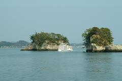 A white ferry boat sails between lush green islands in calm blue waters under a clear sky.