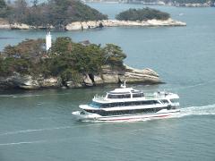 A white ferry boat navigates the blue sea near rocky islands covered in trees.