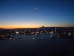 An aerial view of Yokohama's illuminated cityscape and harbor at twilight, with Mount Fuji visible in the distance.