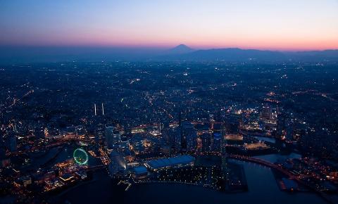 An aerial view of Yokohama city at dusk, with Mount Fuji visible in the distance.