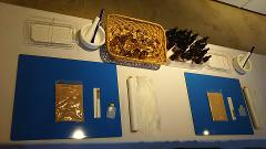 Esta imagen muestra una mesa con ingredientes y herramientas para elaborar remedios herbales. Hay hierbas en una cesta, frascos de extractos, morteros, polvo en bolsas, palillos, recipientes y otros suministros de preparación.