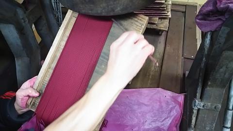 A person uses a thin stick to maneuver bright red incense sticks held in a wooden frame.