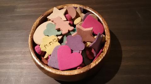 Un cuenco de madera está lleno de una colorida variedad de confeti de papel con formas de corazones, estrellas y otras formas.