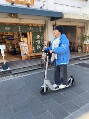 Ise/ Rental Electric Scooter~sacred river route~/90min A person rides a gray electric scooter in front of a shop with Japanese signs.