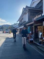 Ise/ Rental Electric Scooter~sacred river route~/90min Two young men ride electric scooters down a picturesque street lined with traditional Japanese buildings.