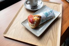 A delicious tote-yaki crepe filled with strawberries and cream sits on a textured grey plate atop a wooden tray, next to a cup of coffee and a golden fork.