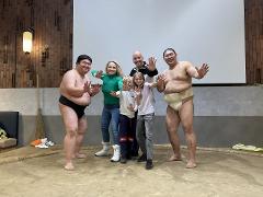 A group of people, including two sumo wrestlers, pose for a photo in a sumo ring at a restaurant.