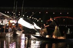 At night, people on boats are fishing with cormorants by the light of a large lantern.