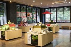 A well-lit store display features various green tea products and sweets, with posters of Japanese snacks and a red umbrella in the background.