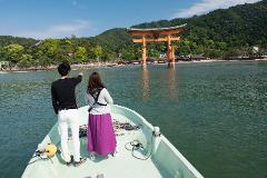 Bir çift, Japonya&#39;nın Miyajima Adası yakınlarındaki denizde duran Itsukushima Tapınağı&#39;nın ikonik turuncu torii kapısını görmek için bir teknede.